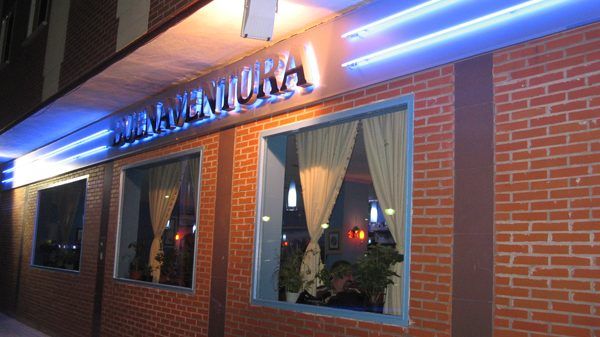 Rótulo metálico con el nombre BUENAVENTURA iluminado por tubos de neón azul sobre la fachada de ladrillo.