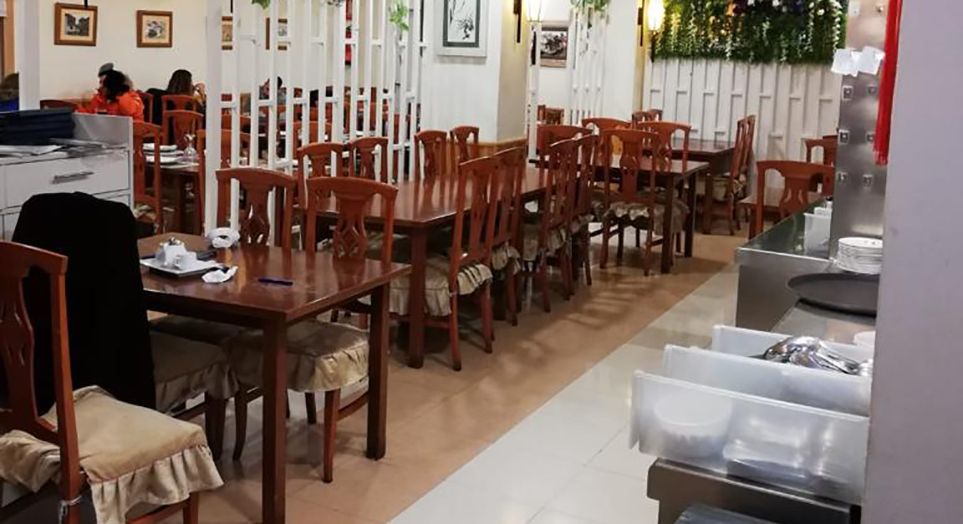 Comedor del restaurante con mesas y sillas de madera clara alineadas junto a una celosía blanca.